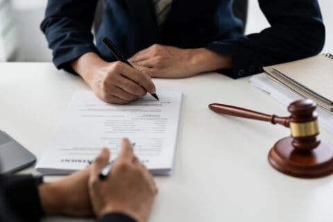 An attorney guiding a client signing paperwork sitting at a table