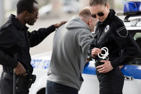 two police officers arresting a suspect next to a police car